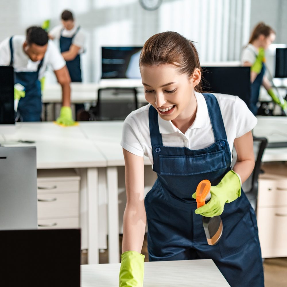 cheerful-cleaner-in-overalls-cleaning-office-desk-with-rag.jpg